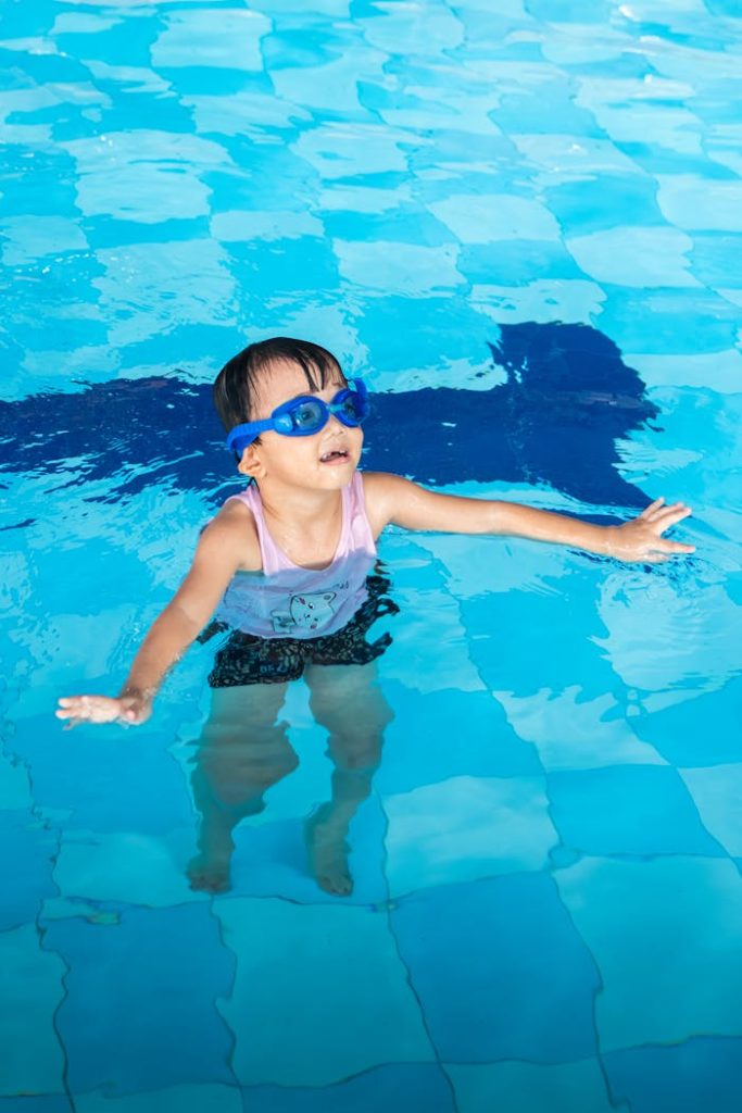 pexels-photo-29195947 A young child wearing goggles enjoys swimming in a clear blue pool on a sunny day.